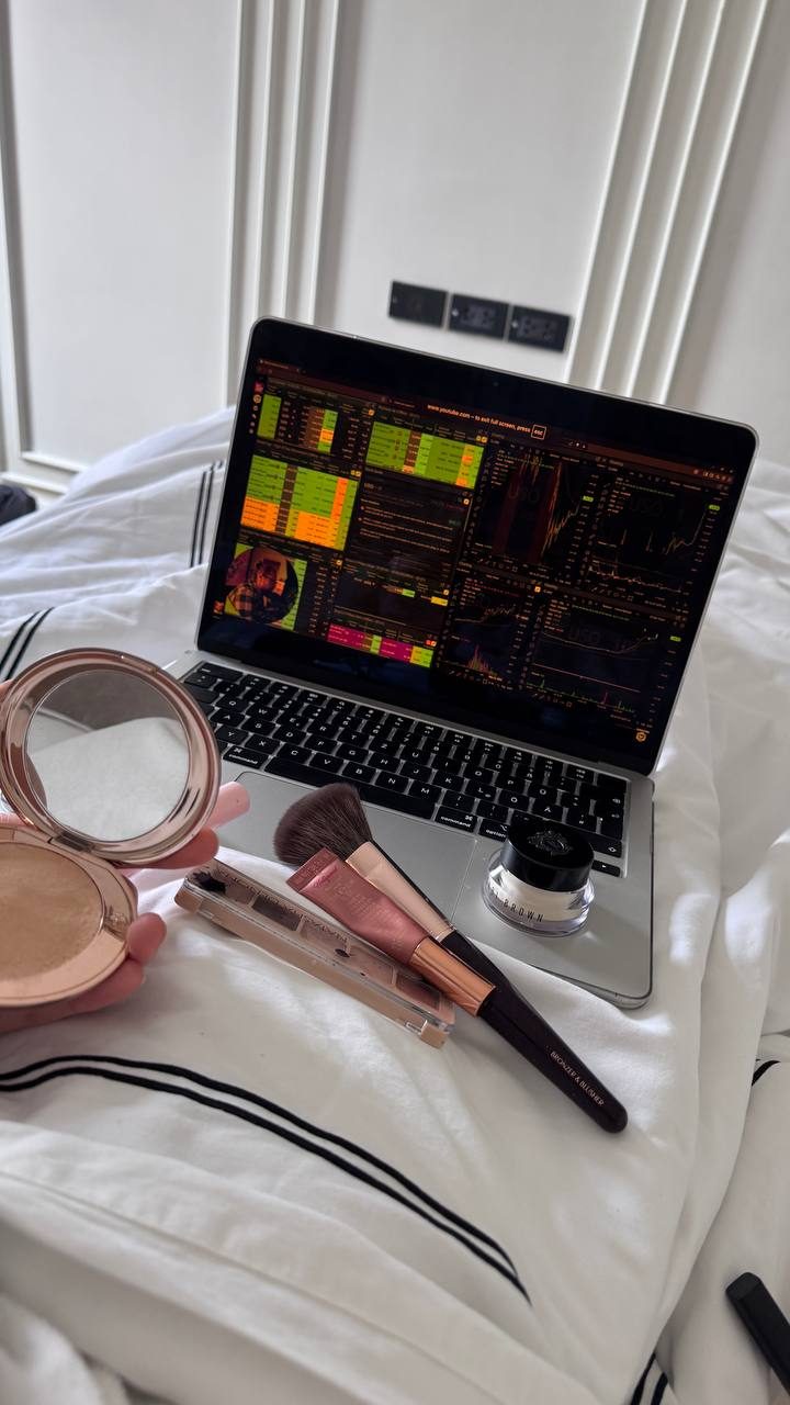 Makeup brushes resting on a laptop showing a trading terminal